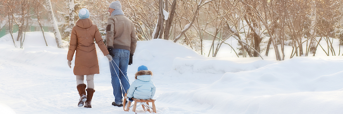 mother and father pulling child through snow on sled