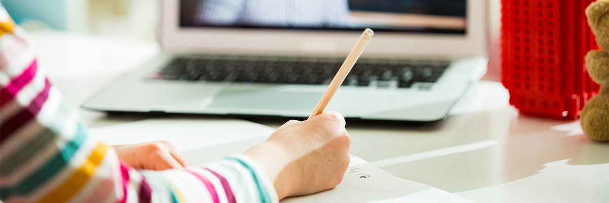 Young child writing in a notebook with computer in background
